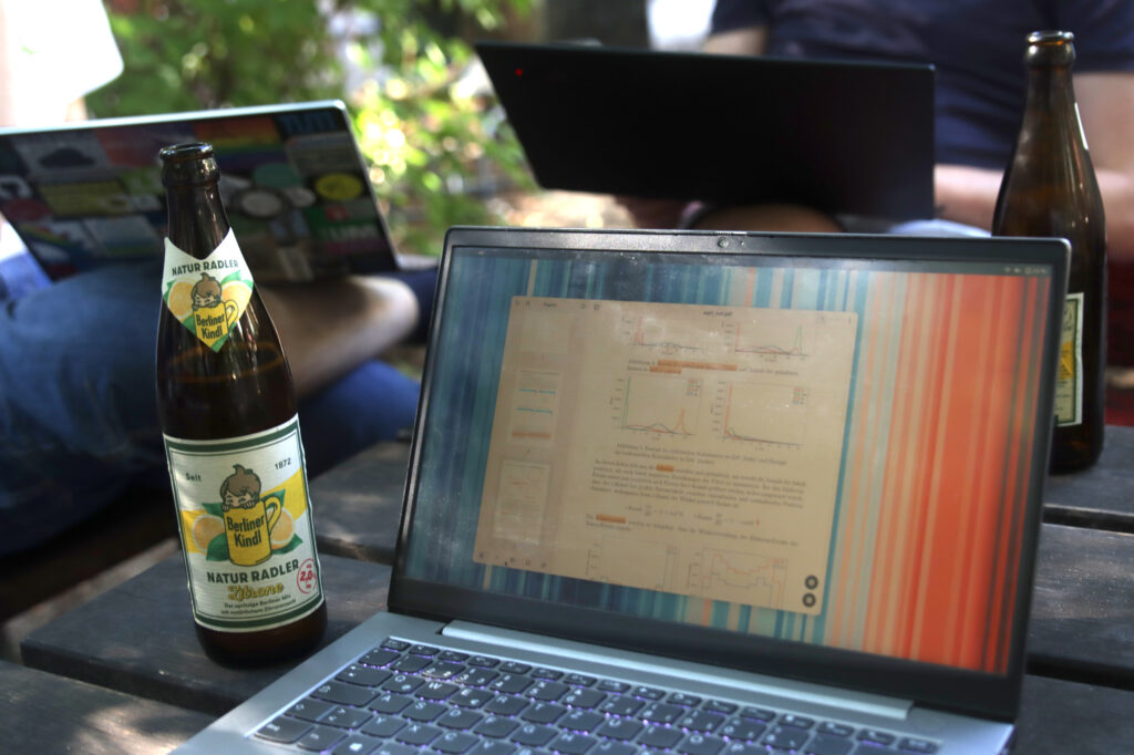 photo of my notebook with Papers open, and a bottle of Radler next to it, with people with notbooks on their laps sitting in the background