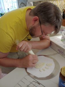 A man in a yellow shirt using an icing bag to pipe the GNOME logo in white.