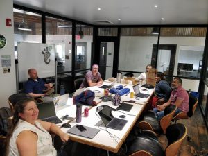 A group of people around a conference room table, covered in things. Everyone is smiling.