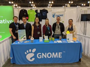 A photo of six people standing behind a table with a blue GNOME table cloth.