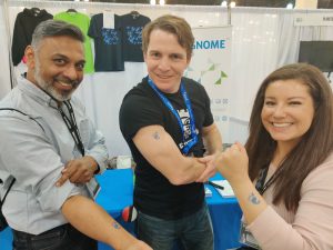 A photo of three people showing off temporary tattoos of the GNOME logo.