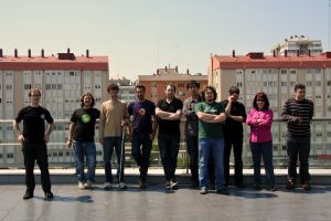 A photo of ten people on a rooftop. Some have their arms crossed. They look Very Serious.