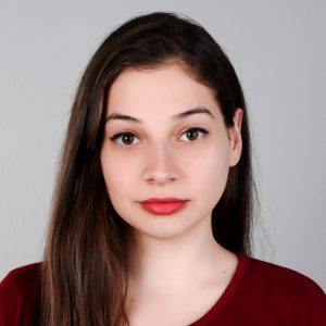 A photo of Kristi Progri. She is wearing a red shirt and fabulous bright red lipstick.