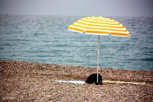 A beach, with blue water, brown sand, and a yellow beach umbrella.