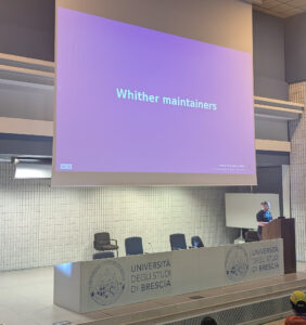 Emmanuele standing in front of a slide that says "Whither Maintainers"