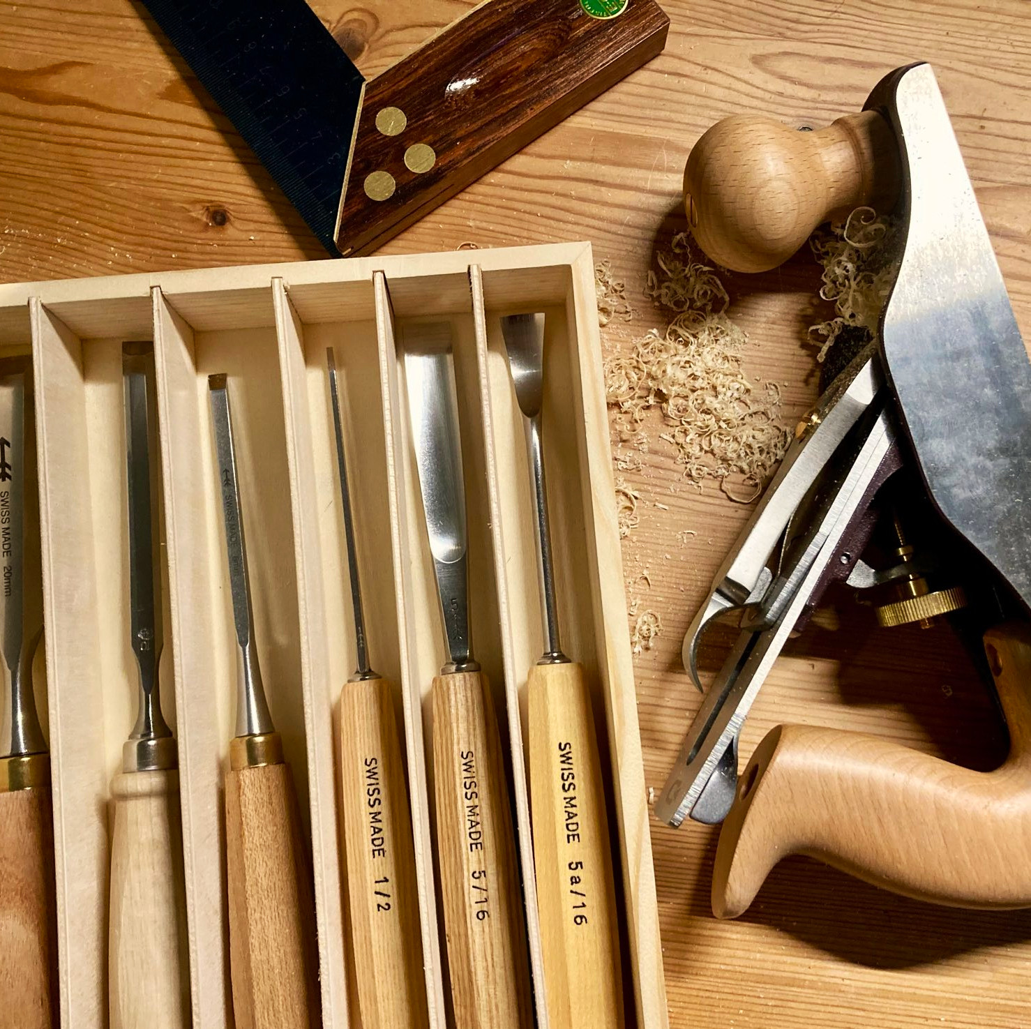 Chisels in a box, carpenter’s square, and a hand plane lying on a table